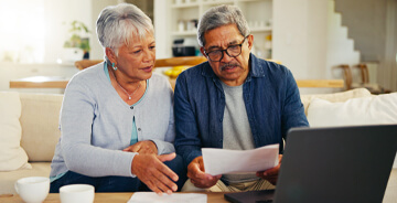 Elderly couple reviewing papers and looking at a laptop screen